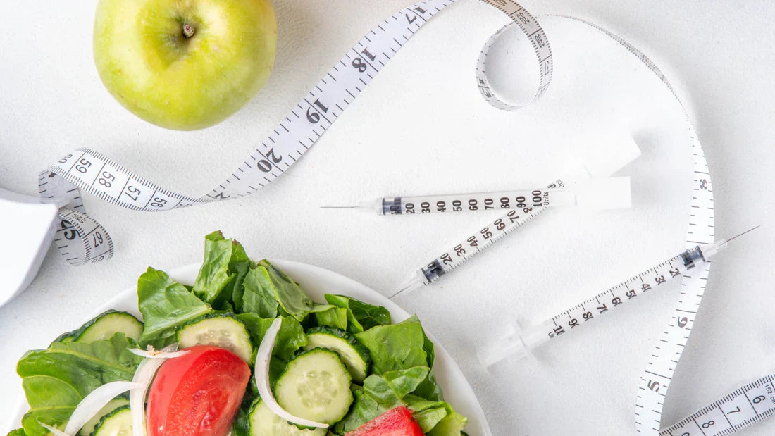 Green apple, a bowl of salad, syringes and a tape measure on a white surface