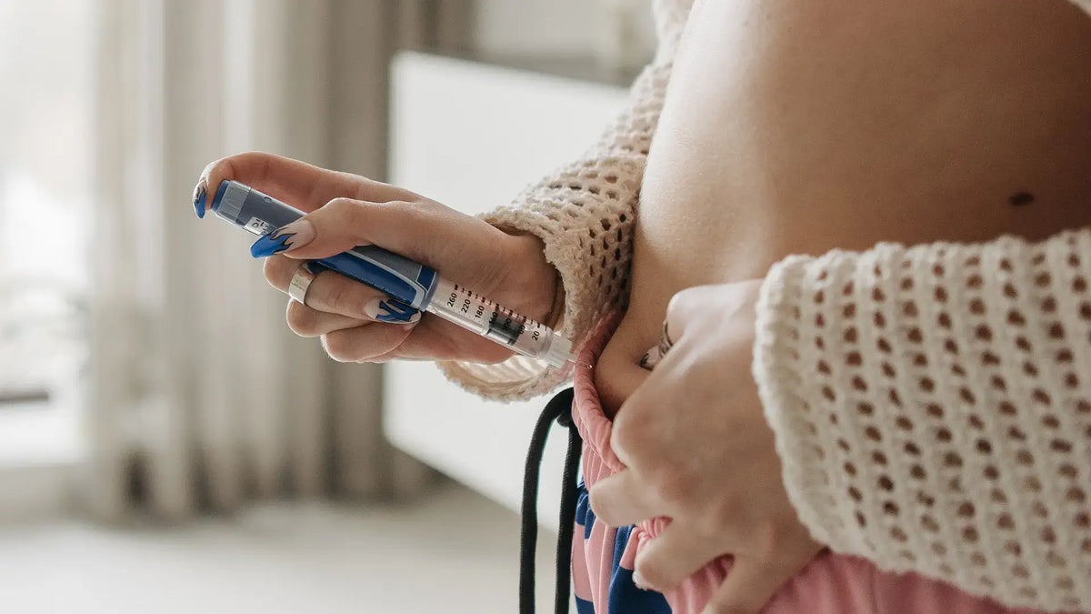 Woman in a cream knit sweater holding an injection pen against her stomach