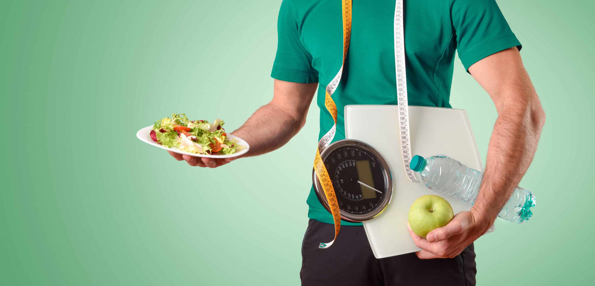Man holding a salad, an apple, a water bottle, a bathroom scale and a tape measure