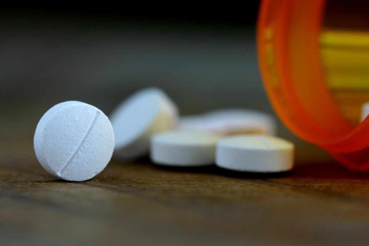 Close-up of white round tablets spilling from an orange pill bottle onto a wooden table