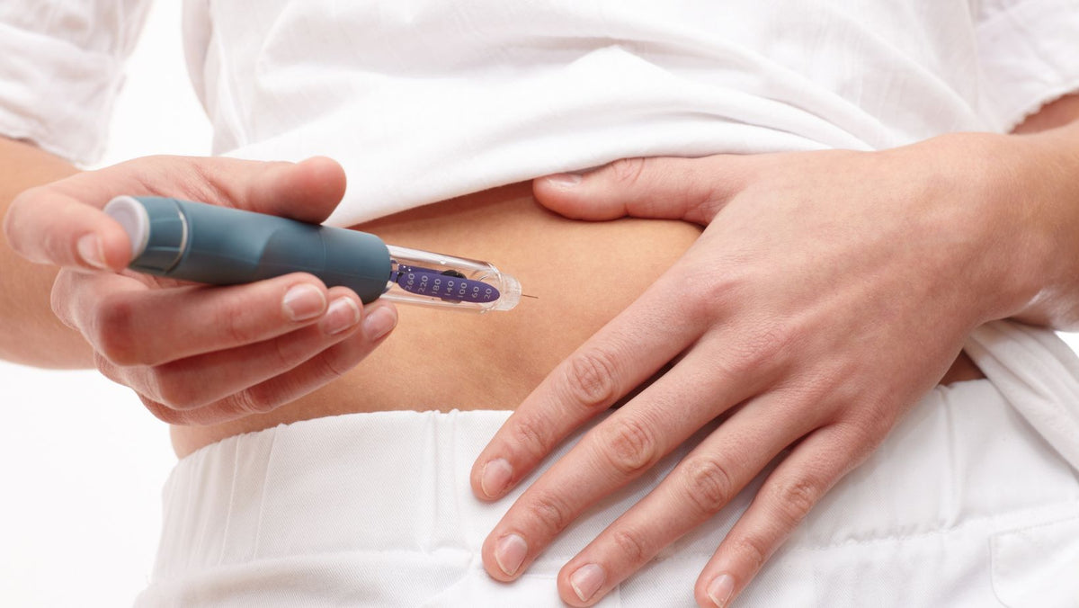 Person lifting a white top and holding an injection pen against their lower stomach