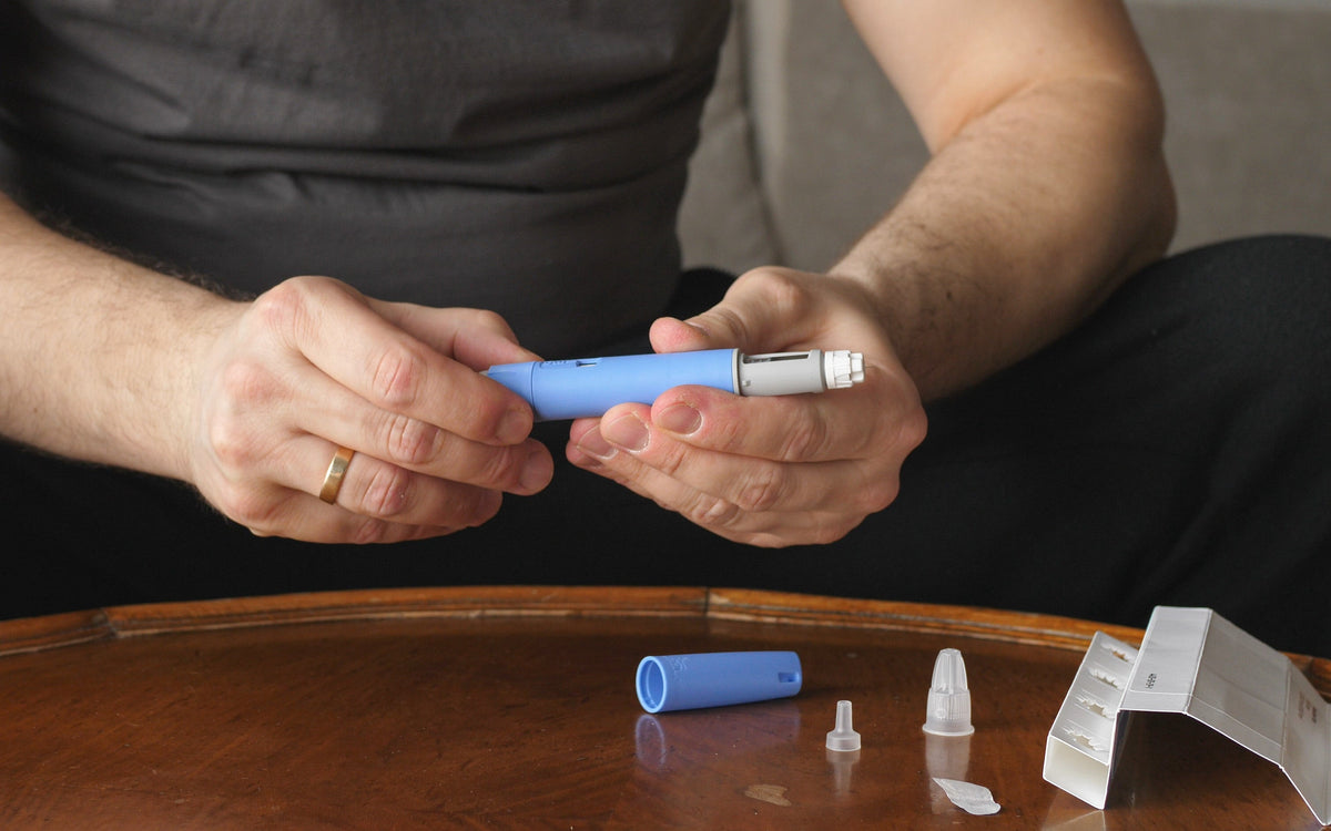 Man holding a blue injection pen with its cap and needle parts laid out on a wooden table