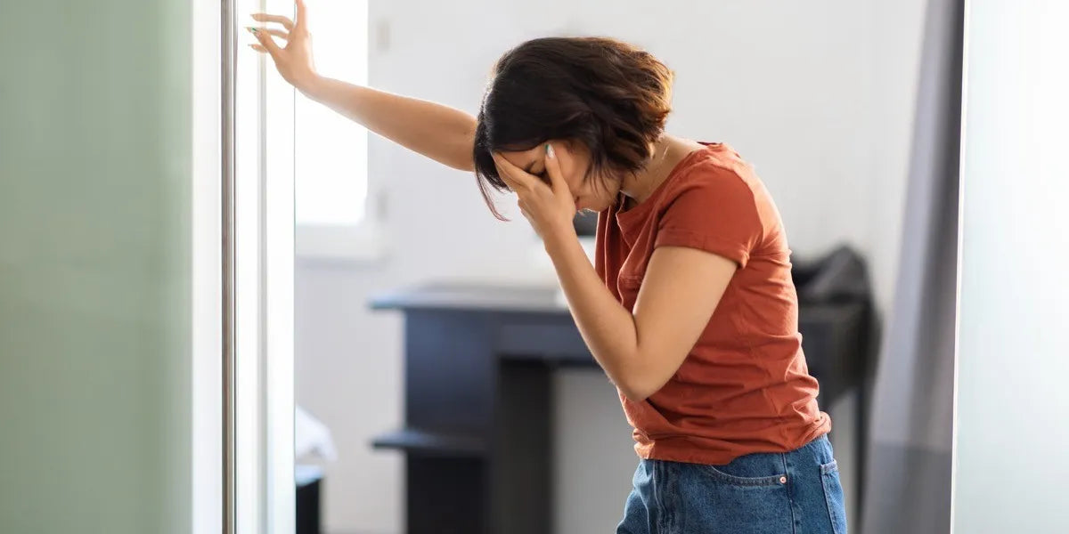 Woman in an orange T-shirt leaning on a door frame and holding her head as if dizzy
