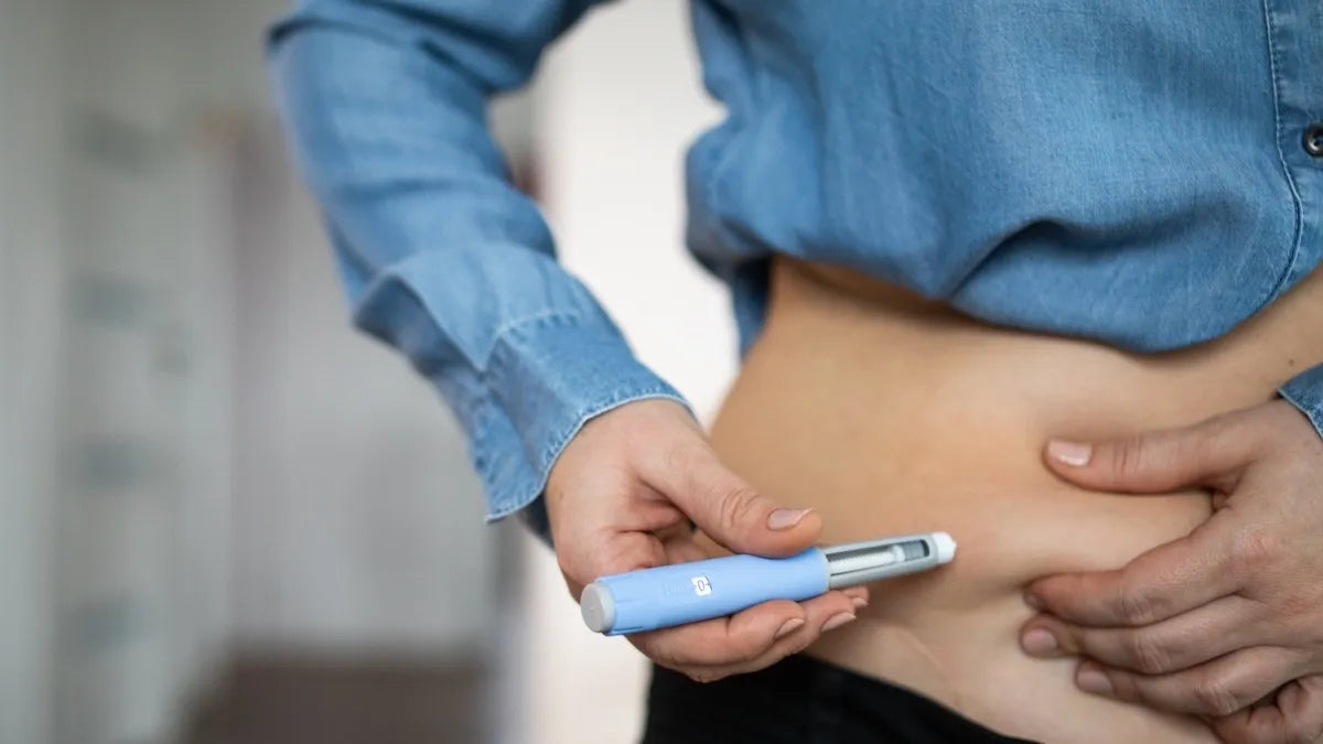 Person in a denim shirt holding a blue injection pen against their stomach