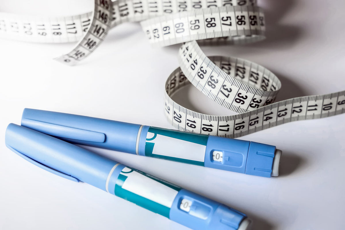Two blue injection pens beside a coiled measuring tape on a white surface