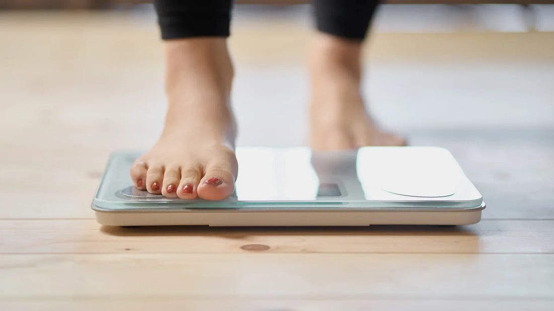 Bare feet stepping onto a glass bathroom scale on a wooden floor