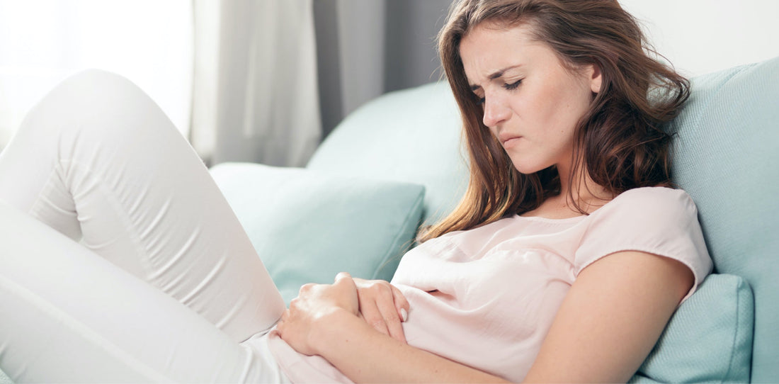 Woman lying on a couch holding her stomach with an uncomfortable expression