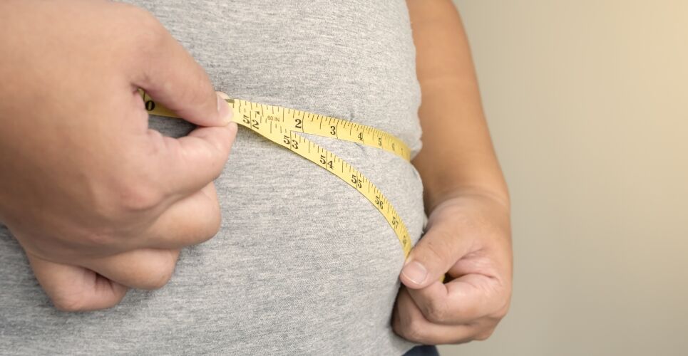 Person in a gray top measuring their waist with a yellow tape measure