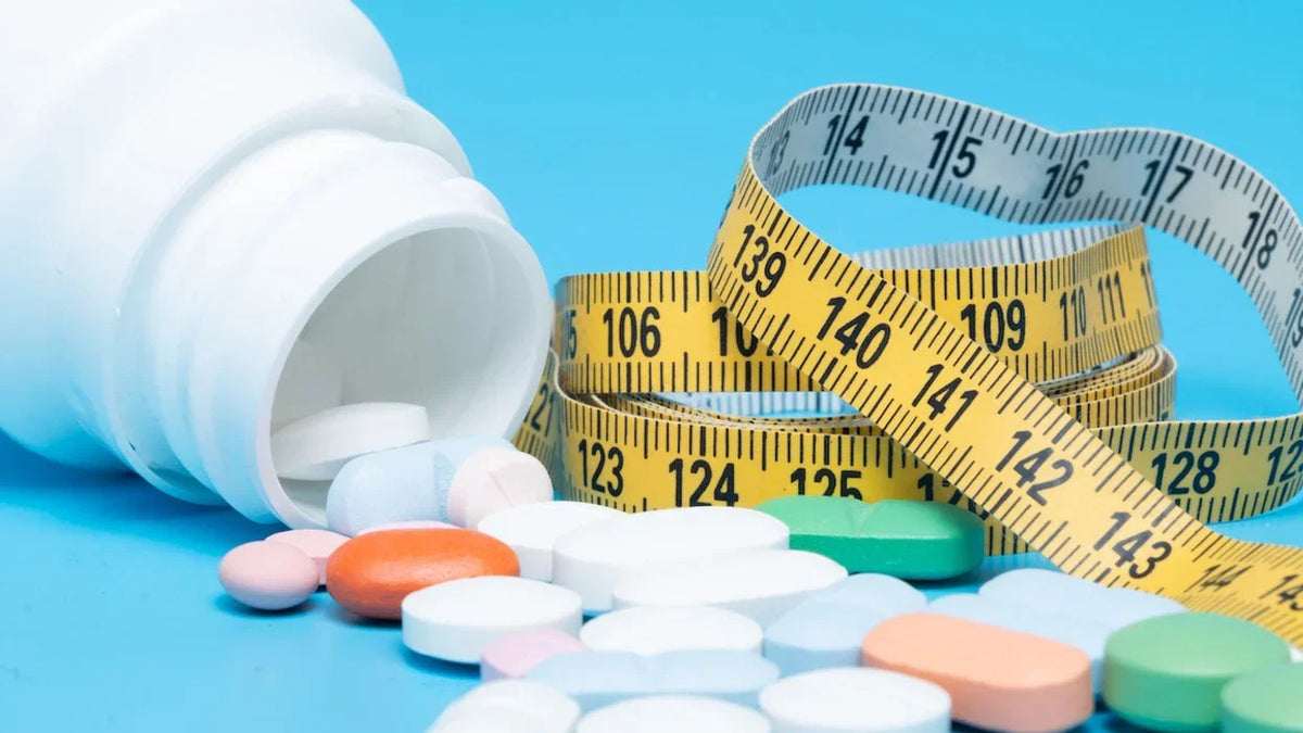 Pills spilling from a white bottle beside yellow measuring tapes on a bright blue background