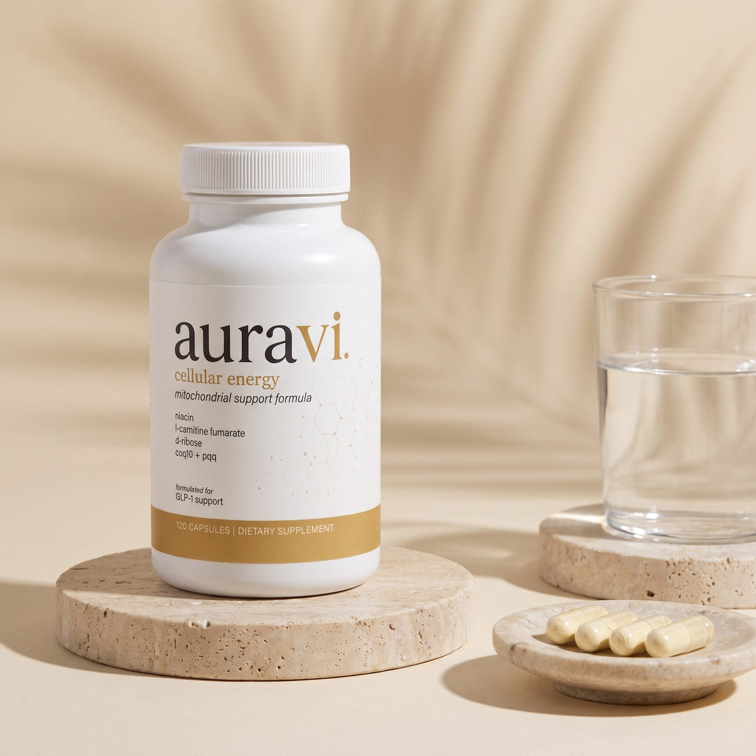 auravi Cellular Energy bottle on a stone pedestal beside a glass of water and capsules