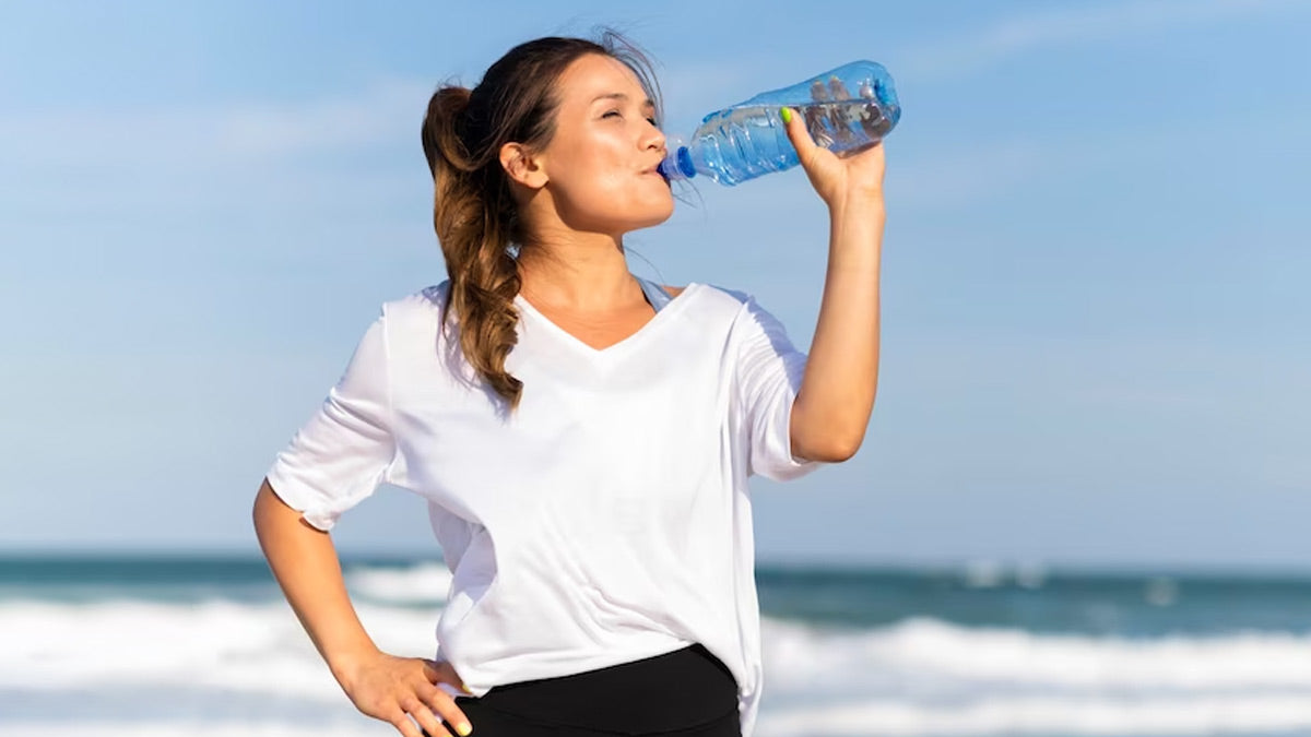 Woman in a white T-shirt drinking from a water bottle on a beach