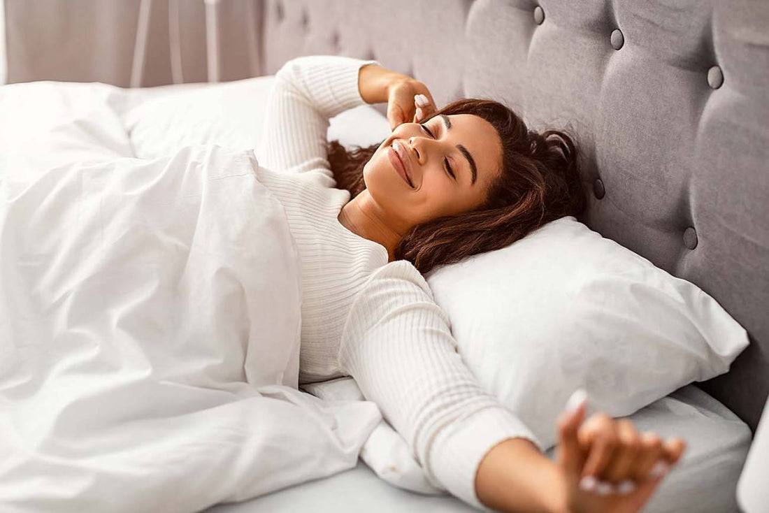 Smiling woman stretching in bed with white sheets after waking up