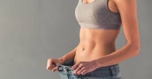 Slim woman in a gray sports bra holding out the loose waistband of her jeans