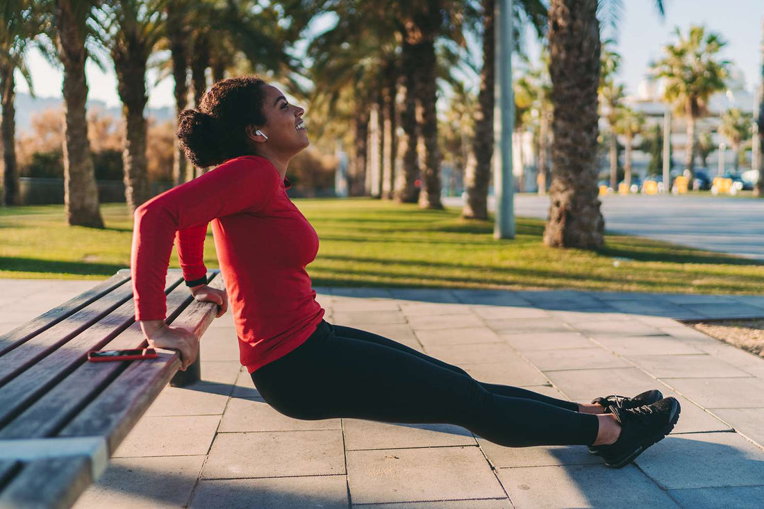Woman in a red top doing bench tricep dips in a palm-lined park