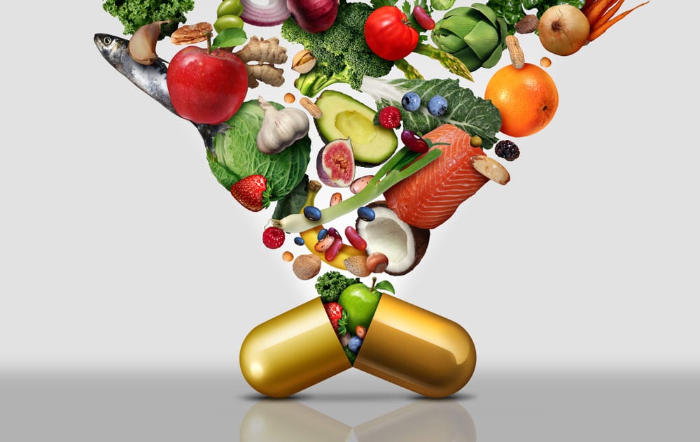 Fruits, vegetables, salmon and nuts pouring into an open golden capsule on a gray background