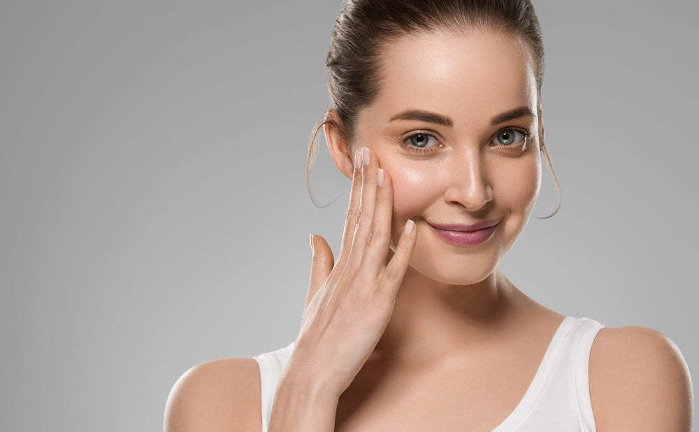 Smiling woman with her hair pulled back touching her cheek against a gray background