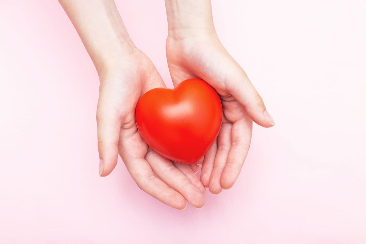 Cupped hands holding a red heart on a soft pink background