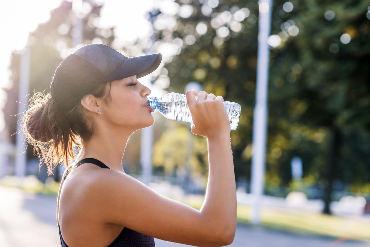 Woman in a baseball cap drinking from a water bottle outdoors in a park